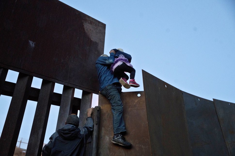 Honduran Migrant helps a young girl across to the American side of the border