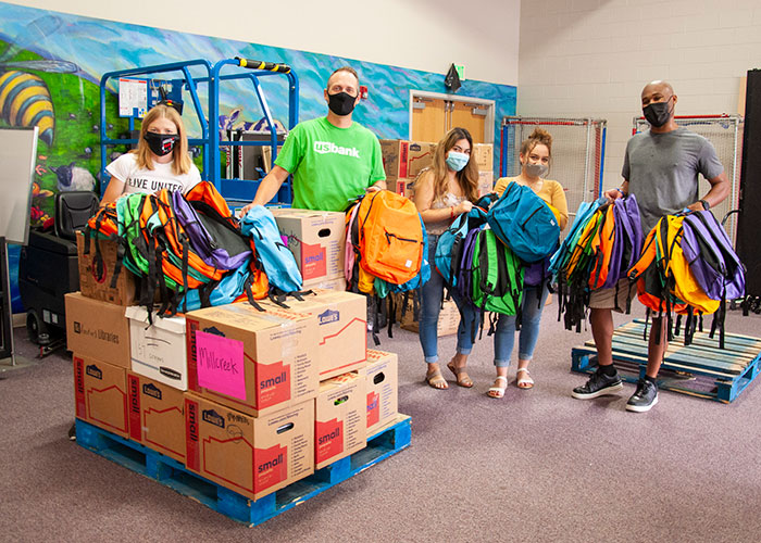 Staff and volunteers hold up colorful backpacks at Stuff the Bus