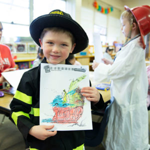 Kindergartner proudly holds up coloring in classroom