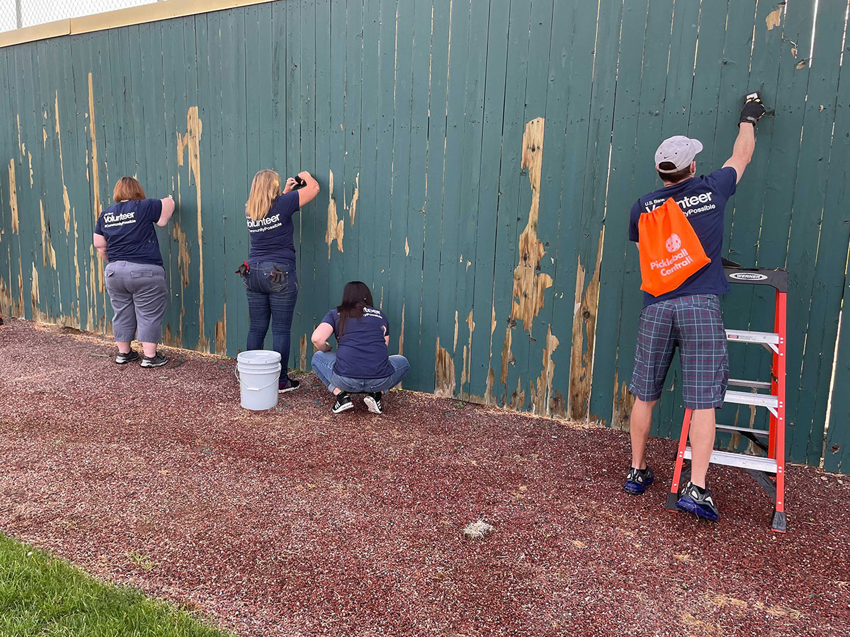 US Bank volunteers paint green fence